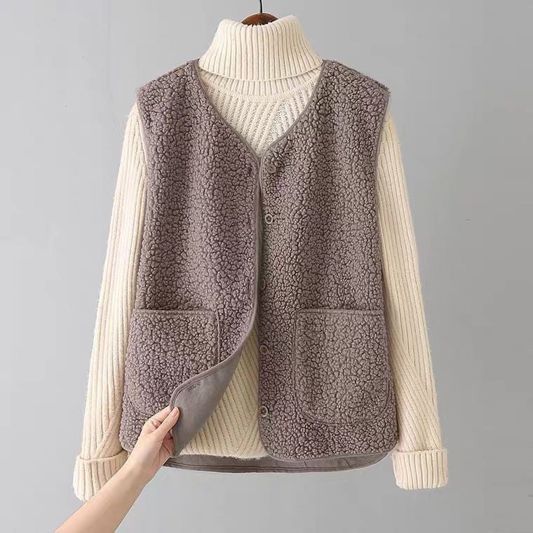 Plush gray sleeveless cardigan with patch pockets over a cream turtleneck sweater on a hanger in a simple gray studio.