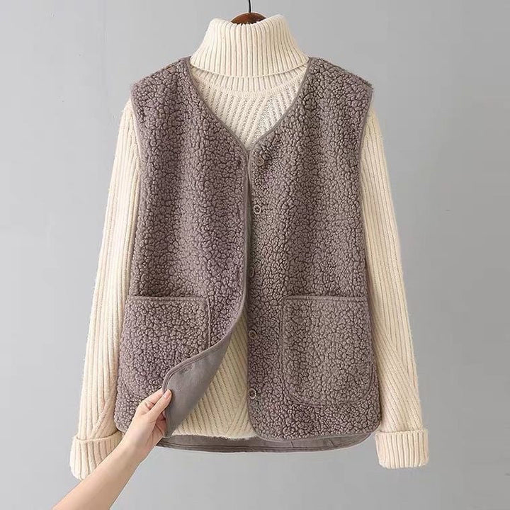 Plush gray sleeveless cardigan with patch pockets over a cream turtleneck sweater on a hanger in a simple gray studio.