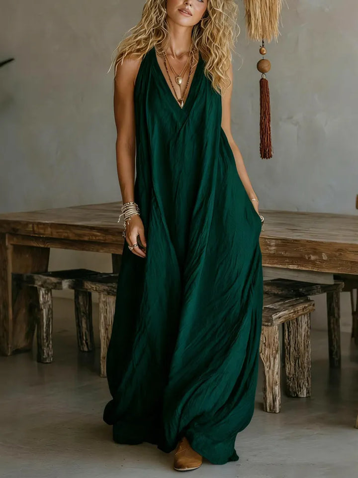 Woman in a flowing green maxi dress in a rustic room with wooden furniture and earth-toned decor.