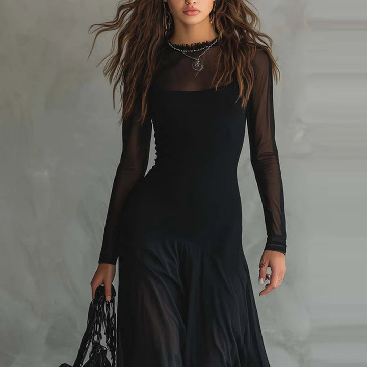 Woman in black maxi dress with long sheer sleeves, holding a bag in indoor setting with textured gray background.