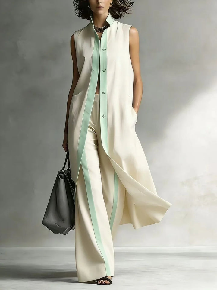 Woman in an ivory sleeveless coat and pants set with mint green trim, carrying a gray bag, in a studio environment.