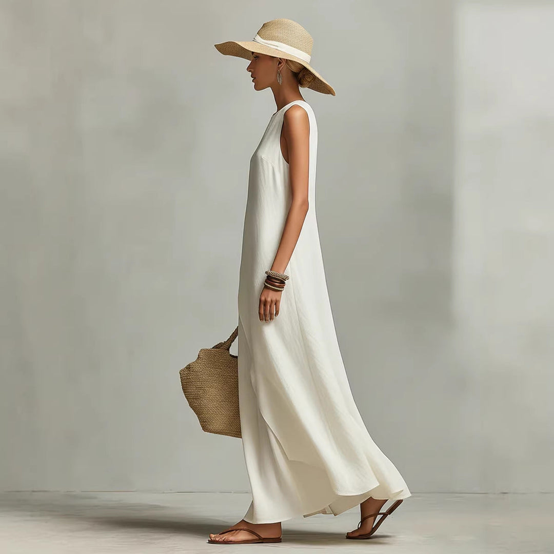 Side profile of a woman in an ivory maxi dress with a hat and woven bag, set against a studio backdrop.