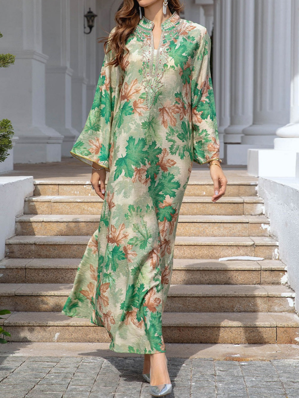 Maxi dress with green maple leaf print worn outdoors on steps in front of classic architectural pillars.