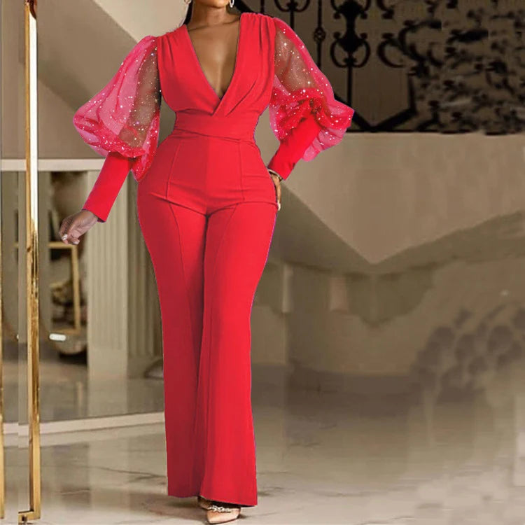 Elegant red jumpsuit with sheer puff sleeves decorated with sparkles, modeled indoors with a staircase backdrop.