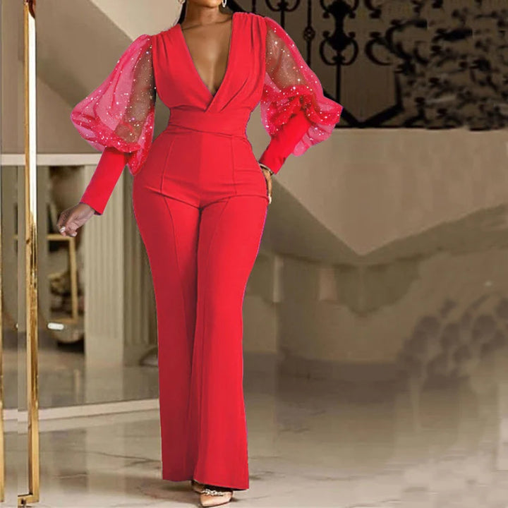 Elegant red jumpsuit with sheer puff sleeves decorated with sparkles, modeled indoors with a staircase backdrop.