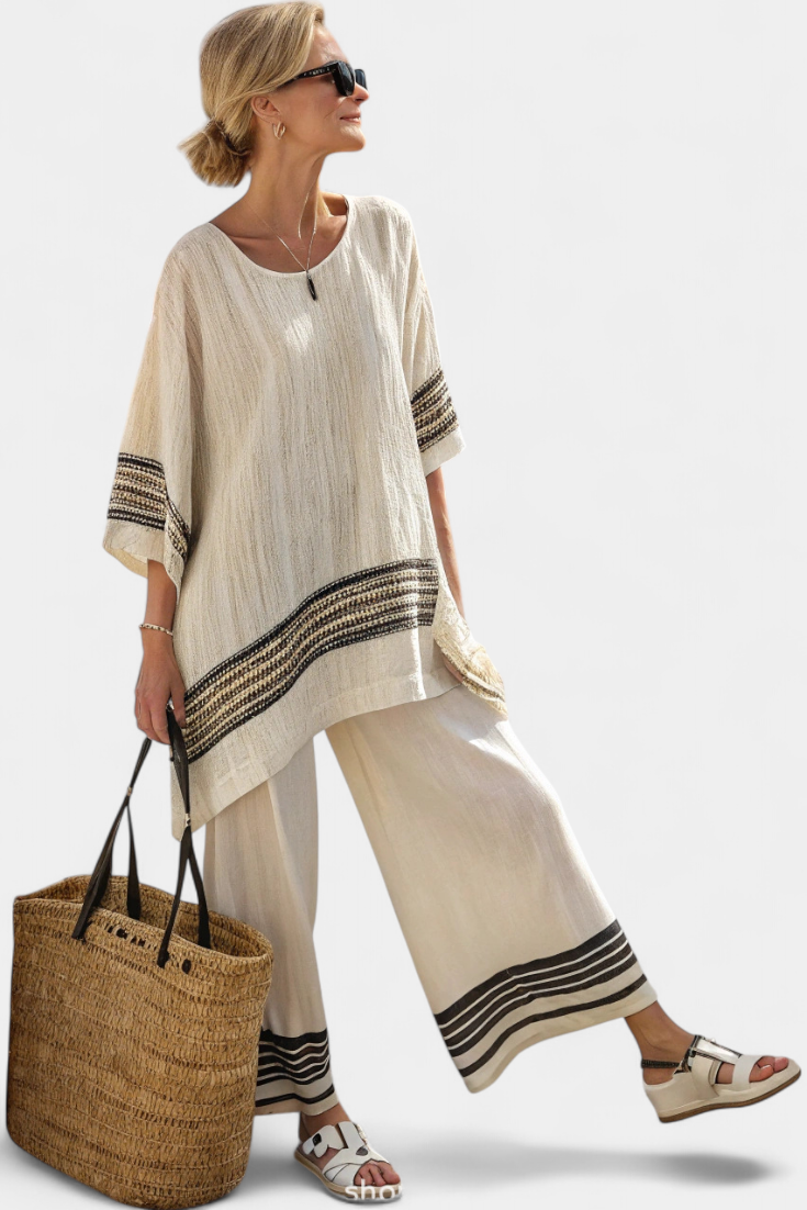 Woman in cream two-piece set with dark stripes, carrying straw bag, wearing sunglasses, neutral background.