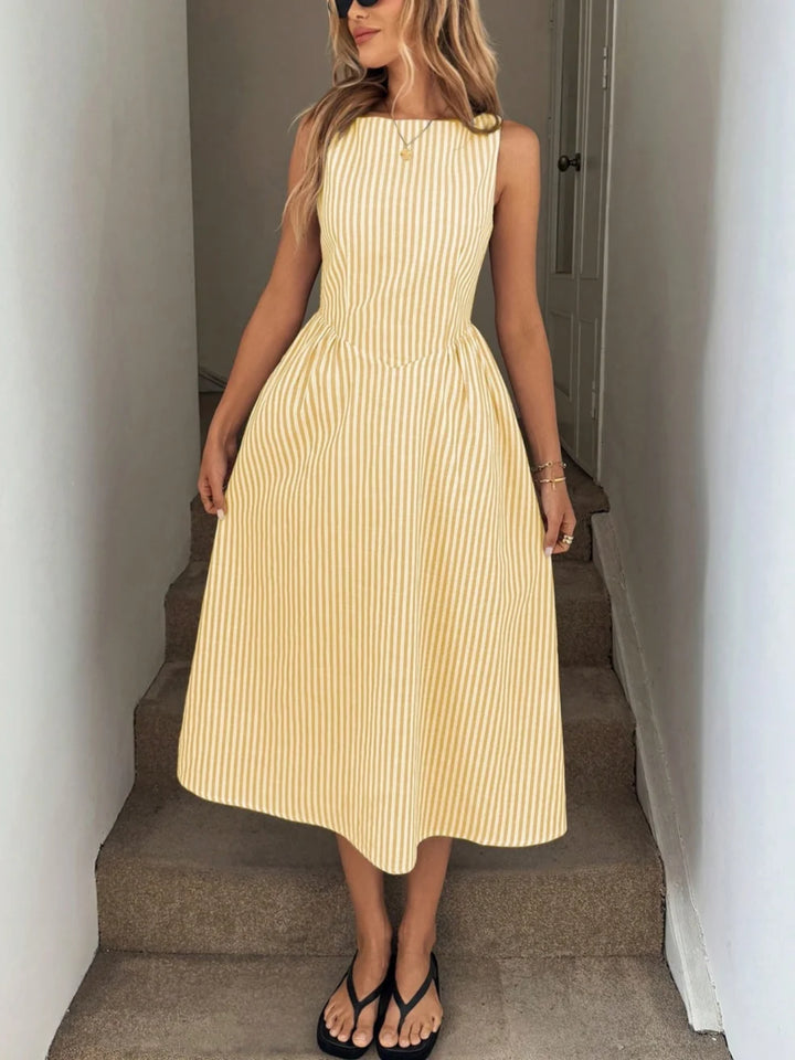 Woman wearing a yellow and white striped maxi dress with a sleeveless design, standing on indoor steps.