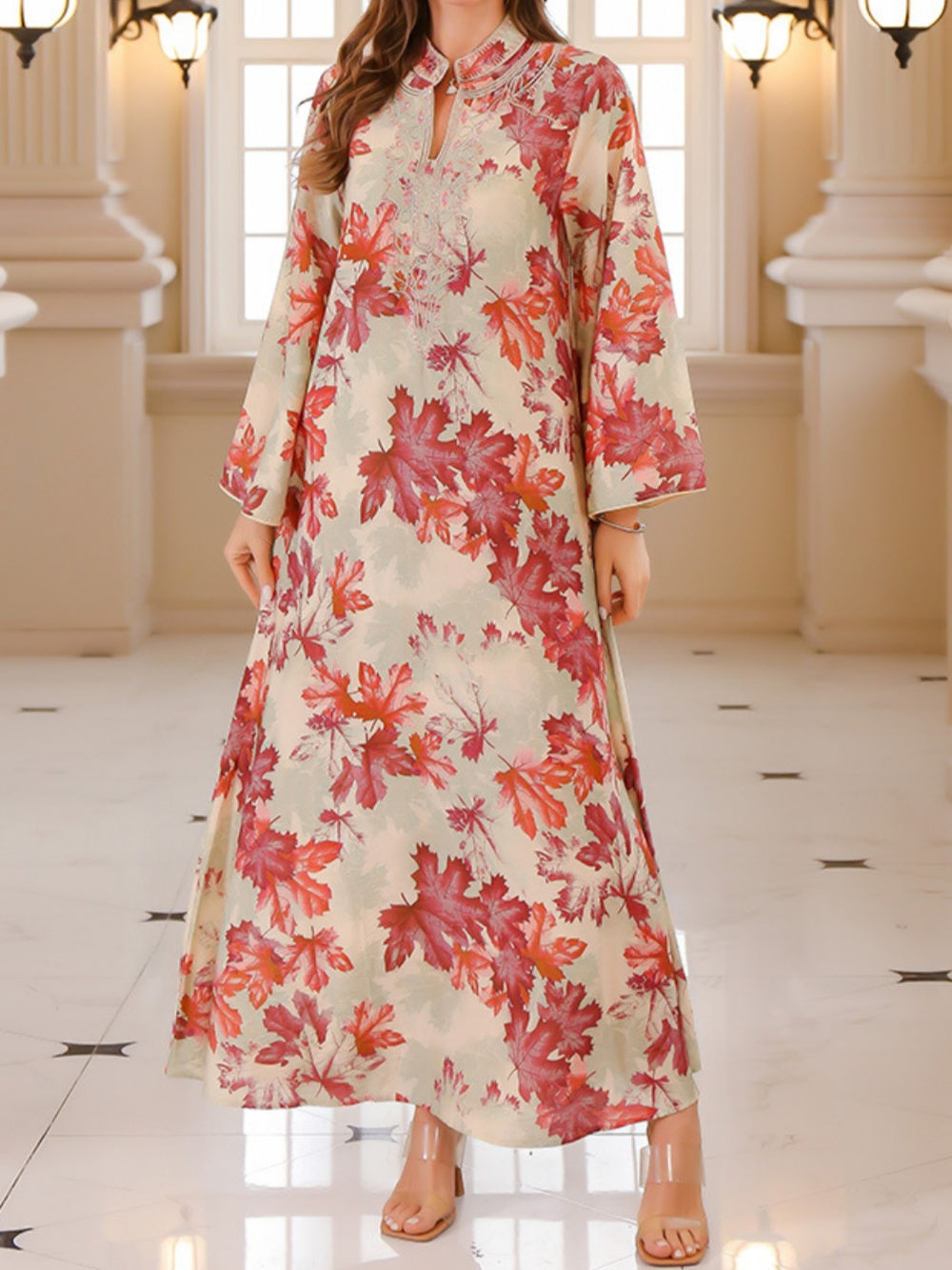 Flowing maxi dress with red maple leaf print, worn indoors with elegant lighting and architecture.