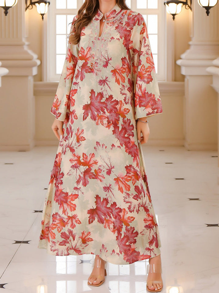 Flowing maxi dress with red maple leaf print, worn indoors with elegant lighting and architecture.