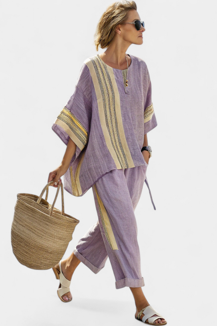 Woman in purple two-piece set with yellow accents, straw tote in hand, sunglasses, against plain backdrop.