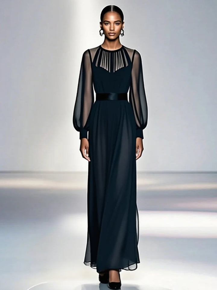 Model in elegant black dress with sheer sleeves, standing in a softly lit studio.