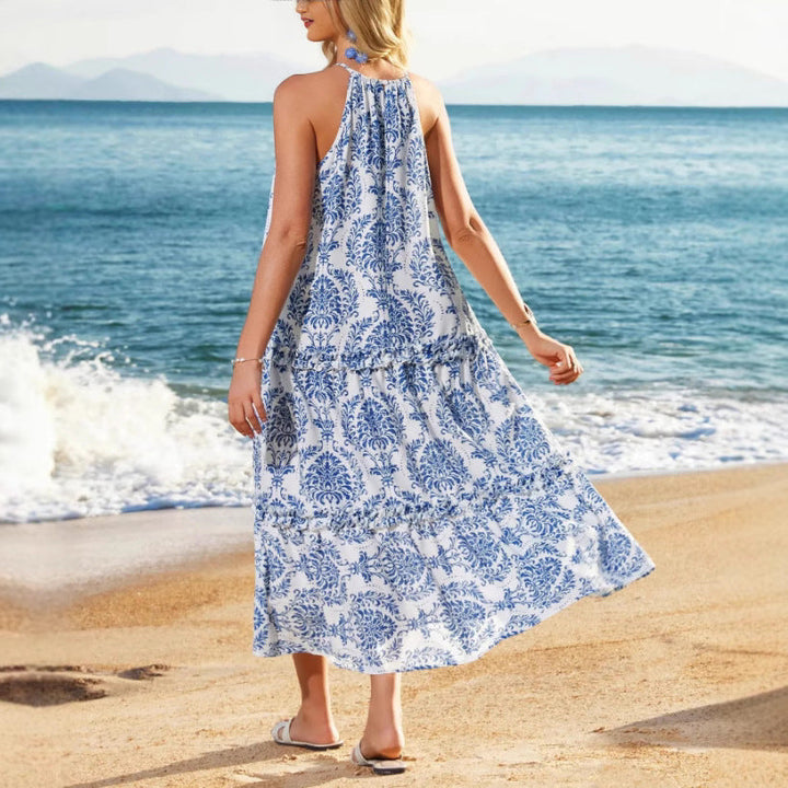 Person wearing a blue and white boho dress standing on the beach, with waves and mountains in the background.