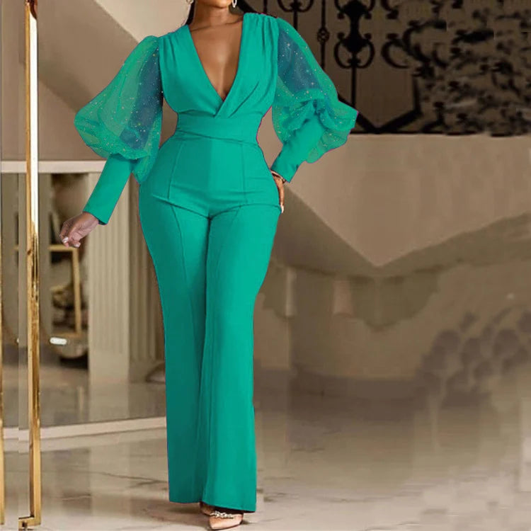 Elegant green jumpsuit with sheer puff sleeves adorned with sparkles, modeled indoors with a staircase backdrop.