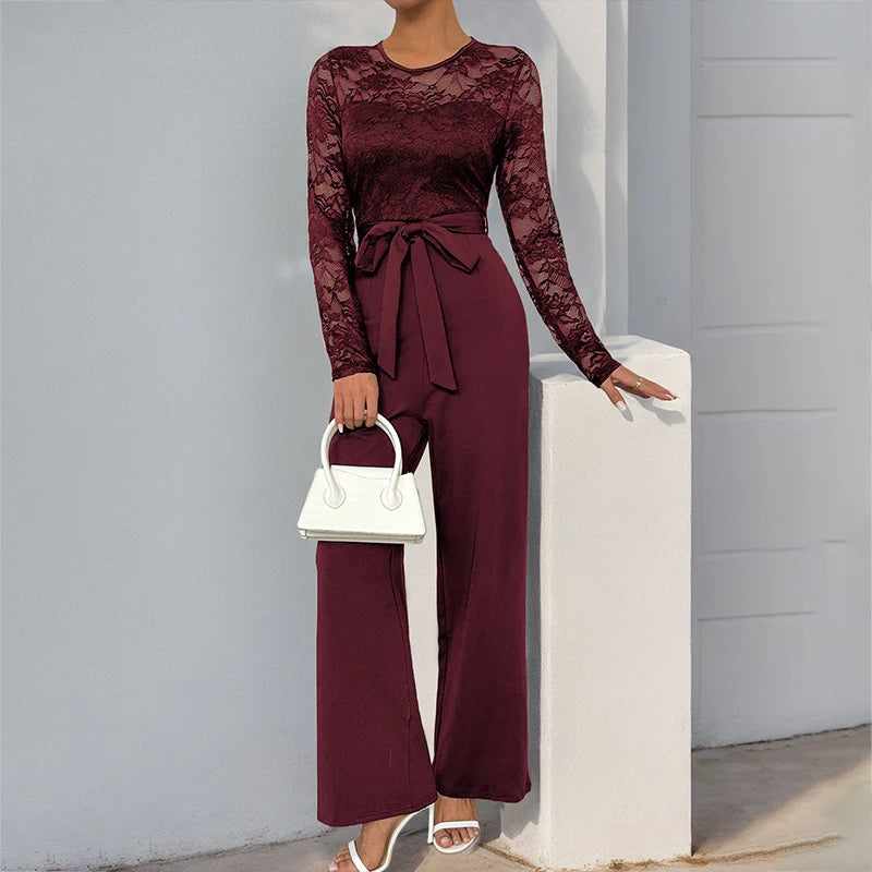 Stylish burgundy jumpsuit featuring lace top and bow waist, holding white purse, outdoor ambiance.