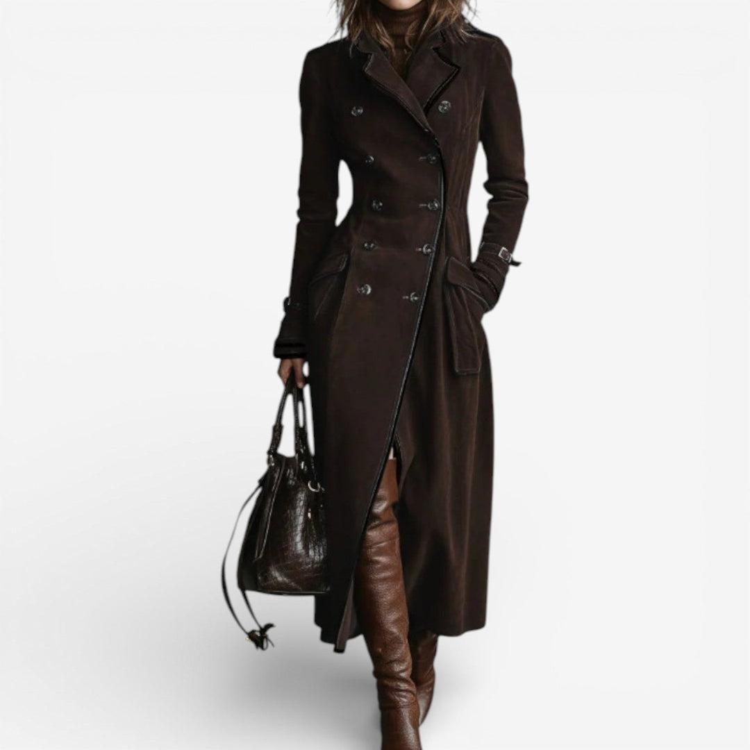 Model in a dark brown suede coat with double-breasted buttons, brown boots, carrying a matching handbag on a plain background.