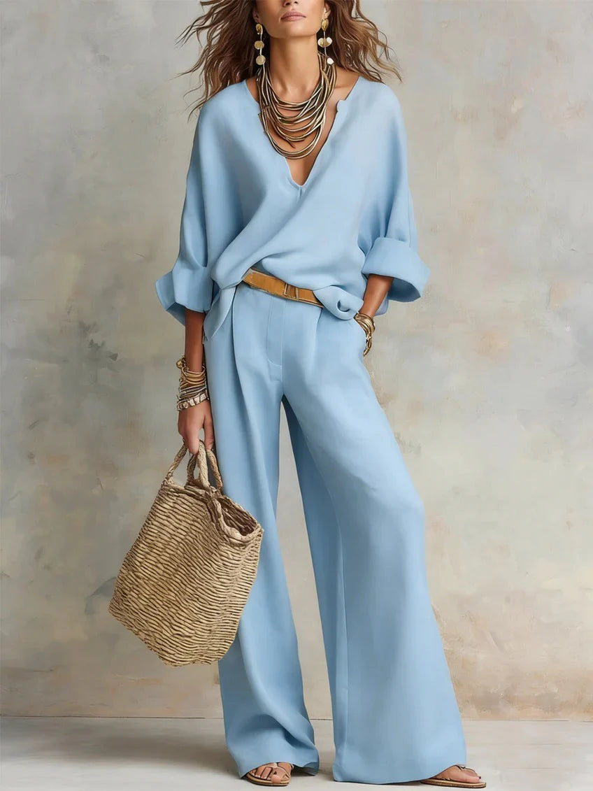 Light blue two-piece set, featuring statement jewelry and a woven bag, shot in a neutral studio environment.