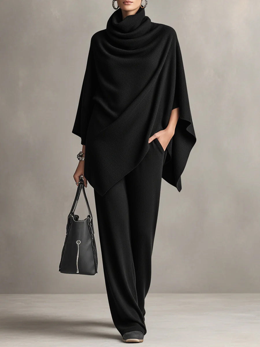 Black two-piece set with elegant draped top and wide-leg pants in studio setting, accessorized with black handbag.