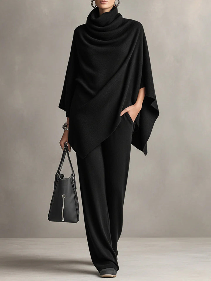 Black two-piece set with elegant draped top and wide-leg pants in studio setting, accessorized with black handbag.