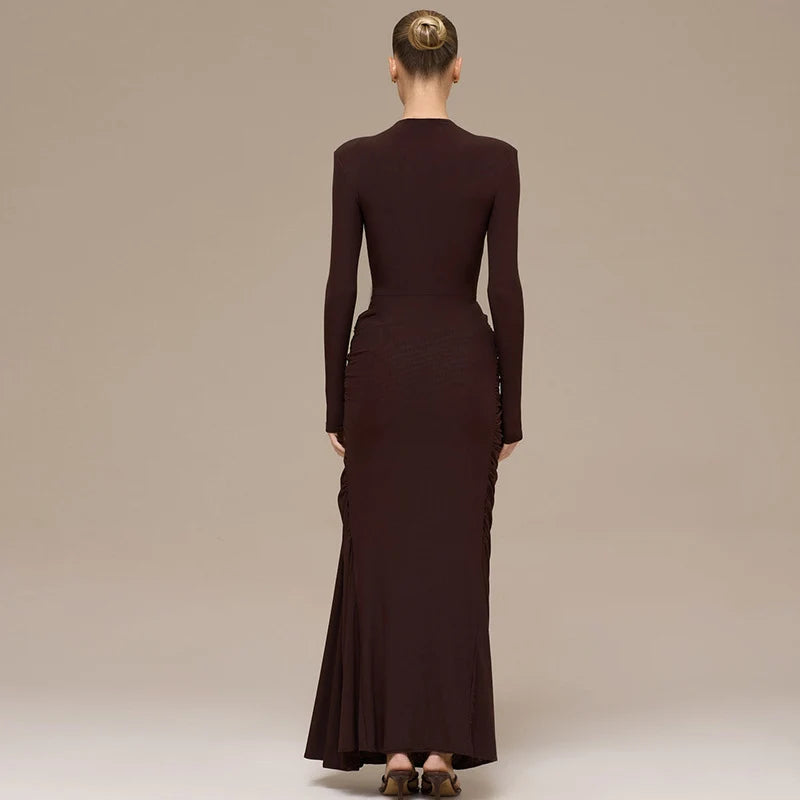 Back view of a woman in an elegant brown maxi dress with long sleeves, posing against a plain studio background.