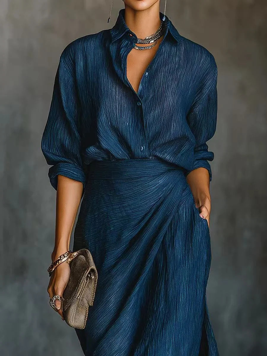Close-up of a blue maxi dress with a buttoned-up top and a necklace, worn with a bracelet and clutch in a studio setting.