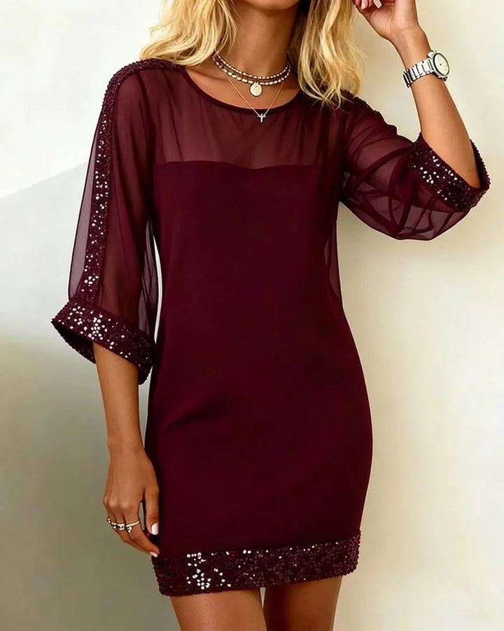 Elegant deep red dress with sheer sleeves and sparkly trim, worn indoors against a light wall.