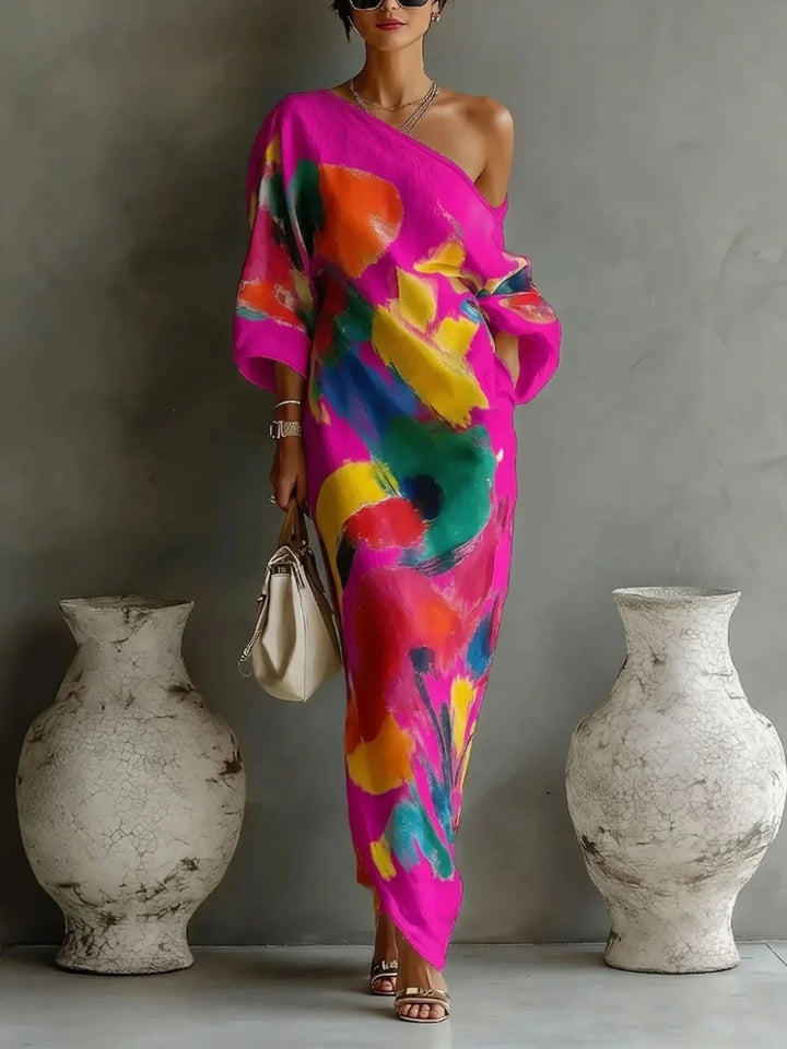 Pink off-shoulder maxi dress featuring bold abstract patterns, complemented with a handbag, in a minimalist indoor setting.