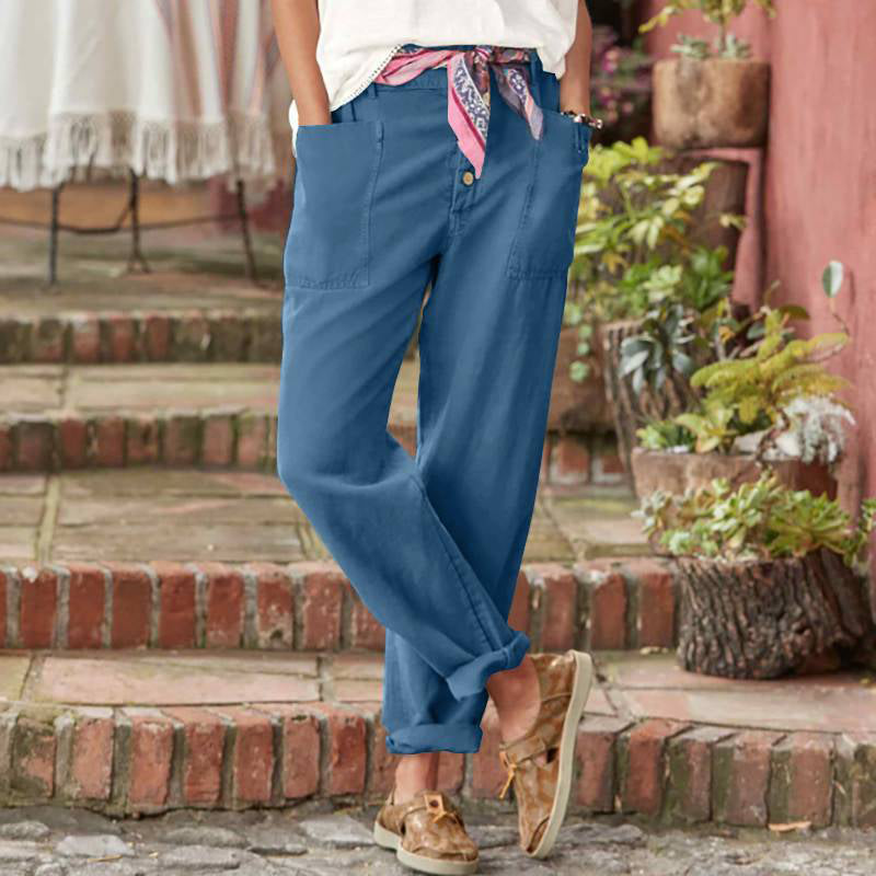 Blue casual pants with button front and scarf belt, photographed in a lush outdoor setting.