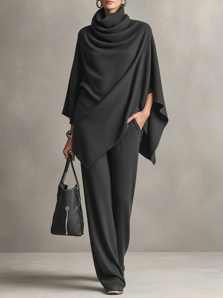 Black two-piece set with elegant draped top and wide-leg pants in studio setting, accessorized with a black handbag.
