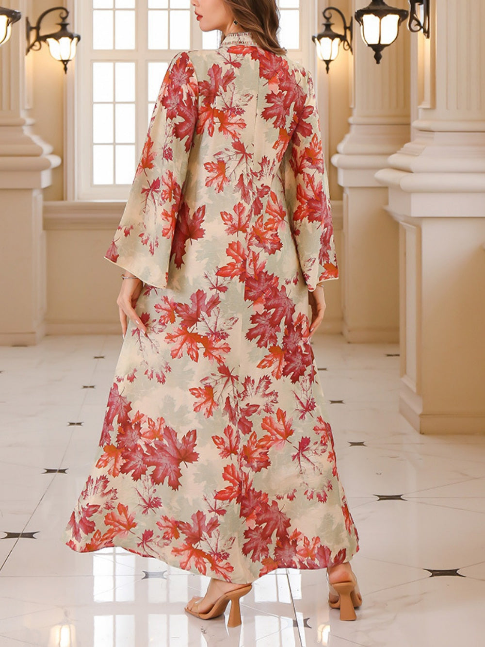 Back view of a flowing maxi dress with red maple leaf print, set in an ornate indoor environment.