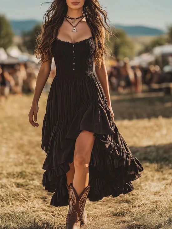 Woman in a black maxi dress with tiered skirt and cowboy boots at an outdoor festival.