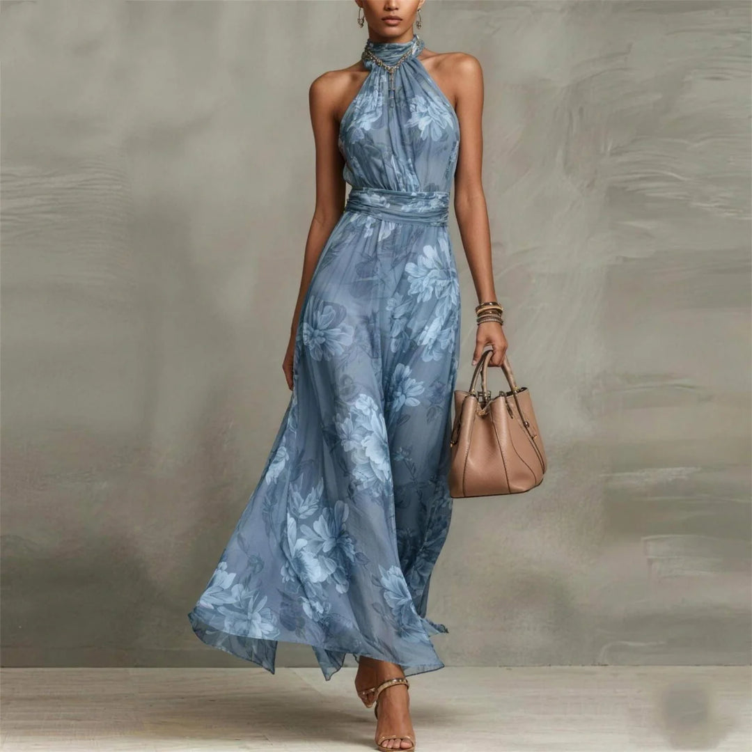 Blue floral halter-neck maxi dress in studio setting with beige handbag.