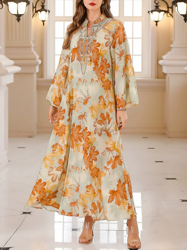 Long maxi dress featuring vibrant orange maple leaf print, modeled indoors with elegant decor.