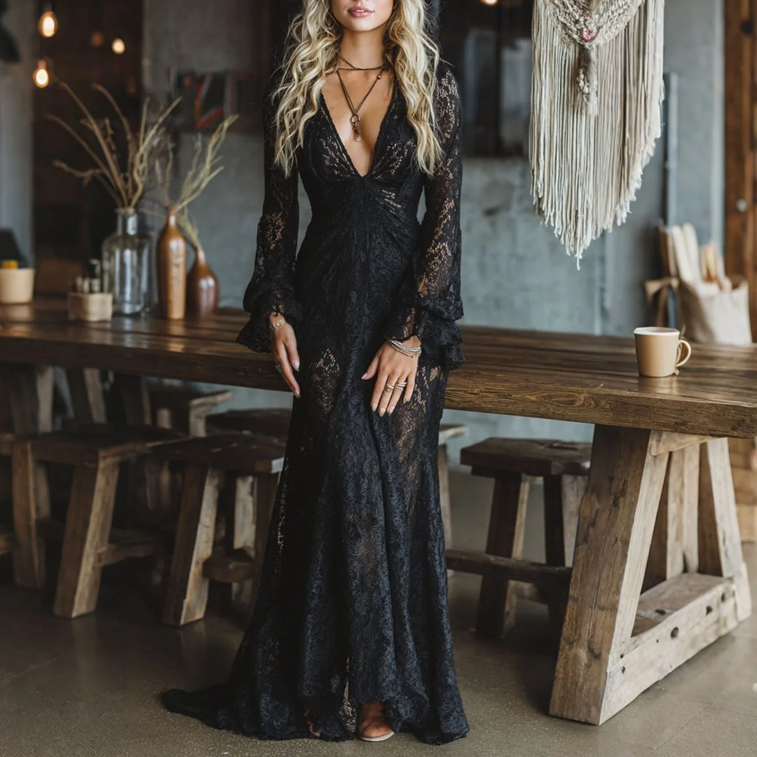 Elegant black lace maxi dress with long sleeves worn by model in rustic setting with wooden table and wall decor.