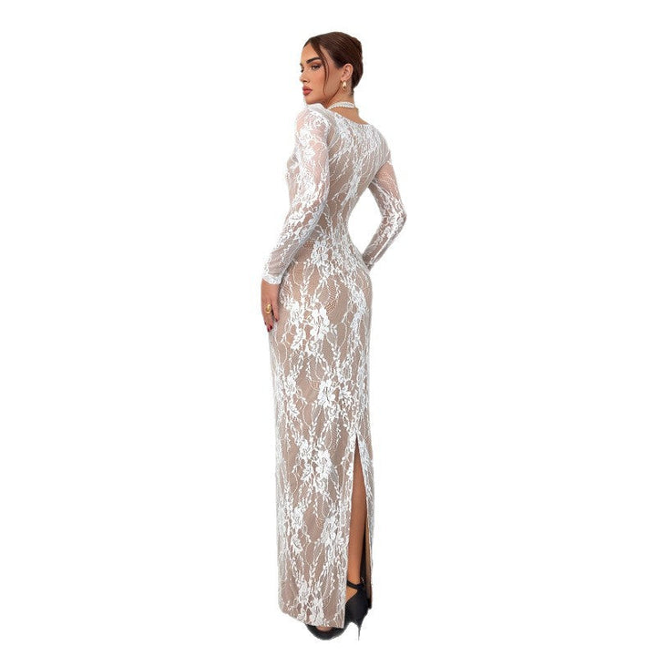 Model in a long white lace dress with delicate floral patterns, standing against a plain white background in a studio.