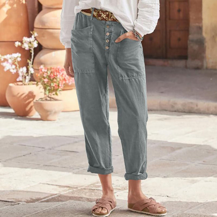 Gray casual pants with button front and rolled cuffs, styled with a white top and sandals in an outdoor setting.