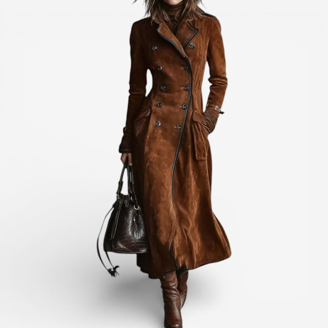 Woman wearing a long brown suede coat with double-breasted buttons and dark boots, holding a dark bag against a white background.