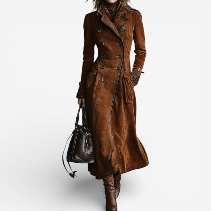 Woman wearing a long brown suede coat with double-breasted buttons and dark boots, holding a dark bag against a white background.