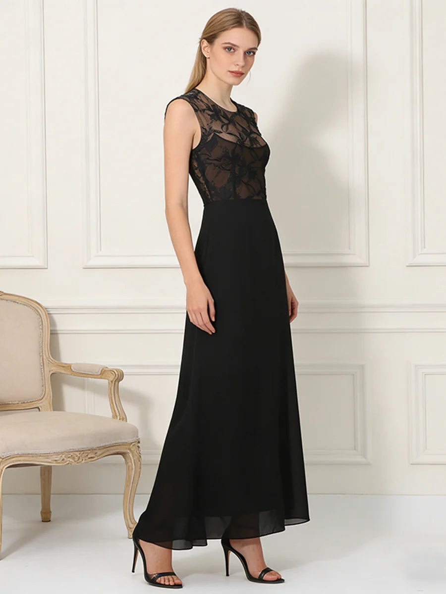 Woman in black dress with sheer lace top and flowing skirt, standing in a classic room with an upholstered chair.
