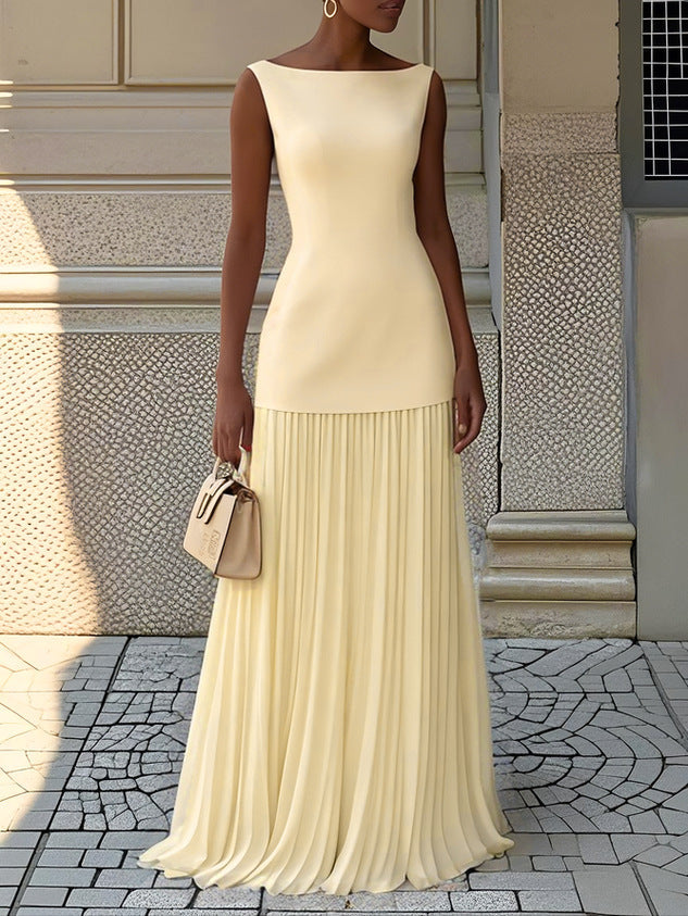 Sunny yellow pleated maxi dress with a tailored top, accessorized with a beige handbag in a modern urban setting.
