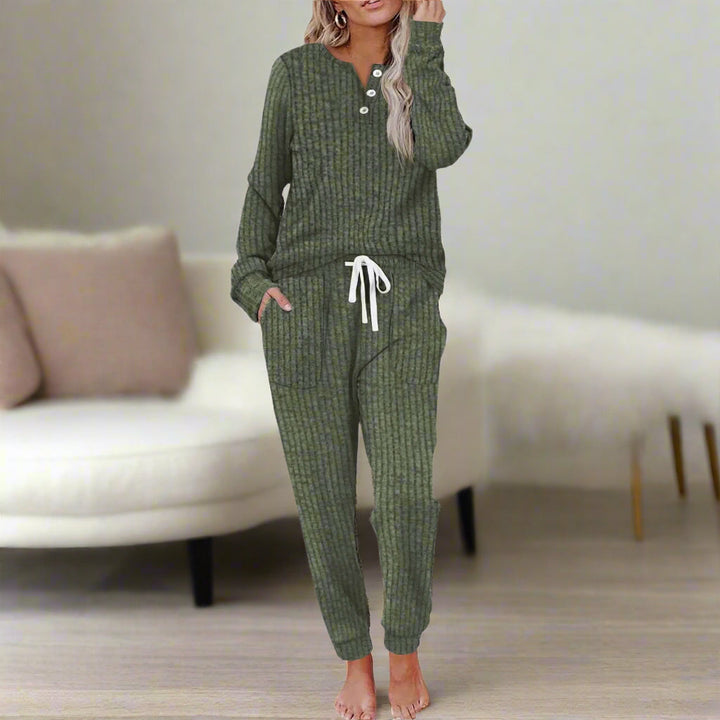 Person in green relax set, standing in a cozy room with a cream sofa and pillows.