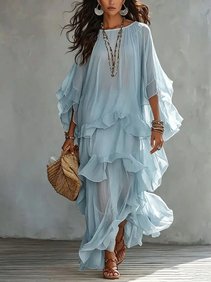 Elegant, layered light blue dress with flowing ruffles and accessories, styled with a straw bag in a studio environment.