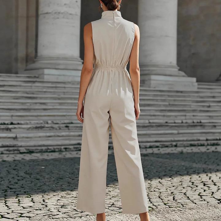 Back view of a cream jumpsuit with a high neckline and cinched waist, set against large stone steps and columns.