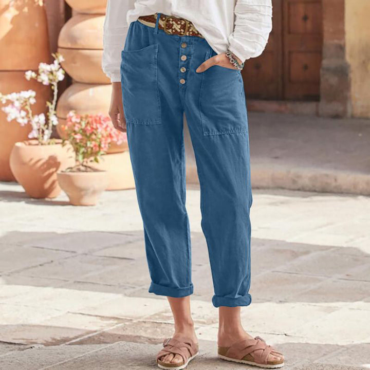 Blue casual pants with button front and rolled cuffs, worn with sandals and a white top in a sunlit courtyard.