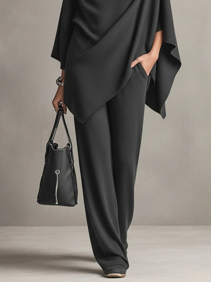 Black wide-leg pants and draped top detail with black handbag in studio setting.