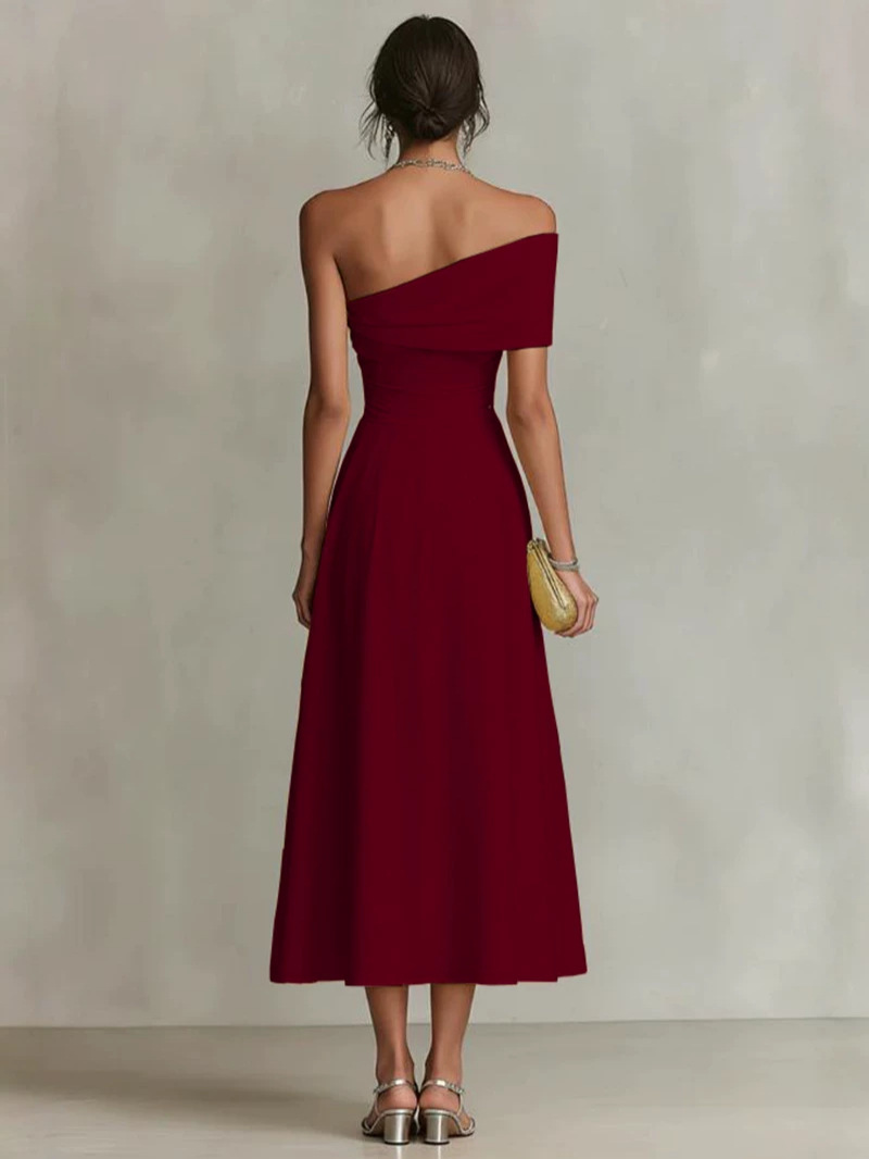 Back view of a woman in a burgundy one-shoulder maxi dress, holding a clutch, in a neutral studio setting.