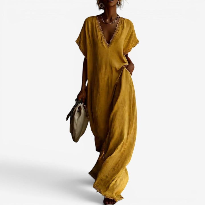 Mustard yellow maxi dress with lace-trimmed V-neckline, modeled by a woman carrying a beige bag against a plain background.