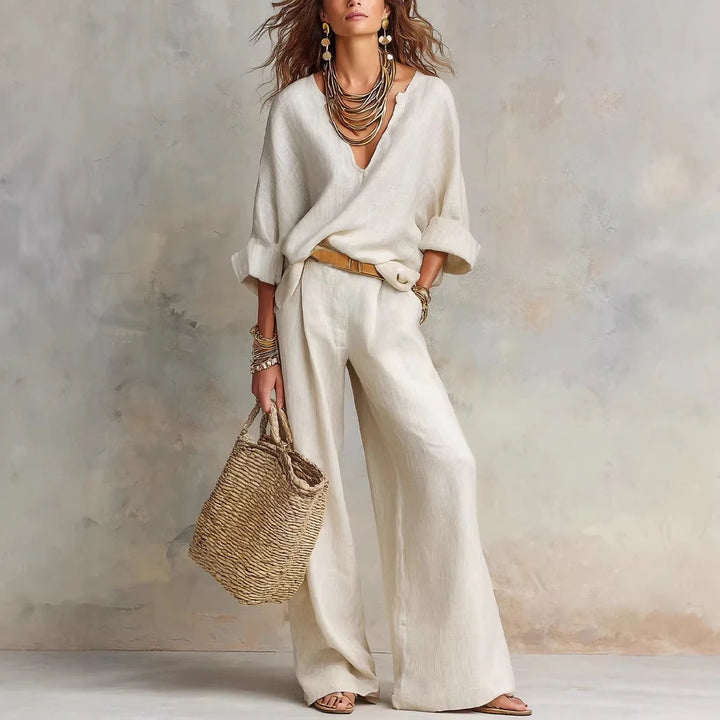 Beige two-piece set styled with statement jewelry and a woven bag in a neutral studio setting.