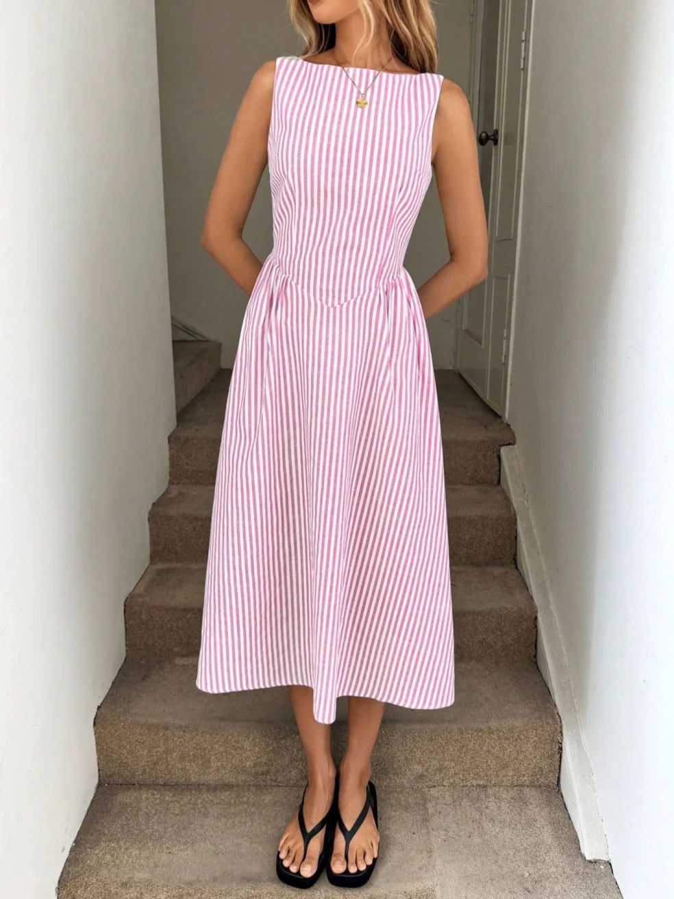 Woman wearing a pink and white striped maxi dress with a sleeveless design, standing on indoor steps.