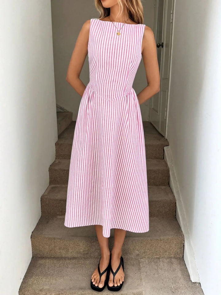 Woman wearing a pink and white striped maxi dress with a sleeveless design, standing on indoor steps.