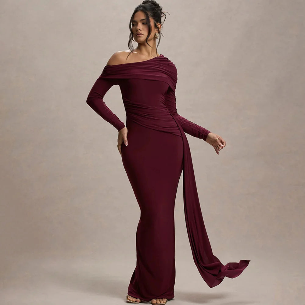 Elegant model wearing burgundy off-shoulder maxi dress with draped detail in studio setting.